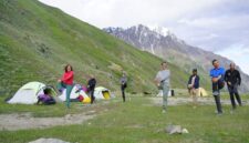 Pemandangan padang rumput pegunungan Tian Shan di Kyrgyzstan dengan tenda tradisional yurt di bawah naungan puncak bersalju.