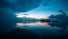 Sebuah kapal kayu tradisional melintas di perairan jernih Labuan Bajo dengan latar belakang perbukitan eksotis Nusa Tenggara Timur saat matahari terbenam.