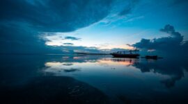 Sebuah kapal kayu tradisional melintas di perairan jernih Labuan Bajo dengan latar belakang perbukitan eksotis Nusa Tenggara Timur saat matahari terbenam.