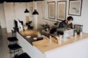 Seorang pelancong menikmati momen santai di sebuah kedai kopi lokal sembari merencanakan rute perjalanan dengan barang bawaan yang ringkas dan efisien.