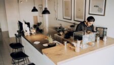 Seorang pelancong menikmati momen santai di sebuah kedai kopi lokal sembari merencanakan rute perjalanan dengan barang bawaan yang ringkas dan efisien.
