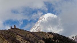Kemegahan Gereja Gergeti Trinity yang berdiri kokoh di atas perbukitan hijau dengan latar belakang lanskap dramatis Pegunungan Kaukasus di kawasan Stepantsminda, Georgia.