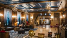 Interior lobi hotel bersejarah berarsitektur klasik yang menampilkan perpaduan lampu kristal dan furnitur kuno terawat rapi.
