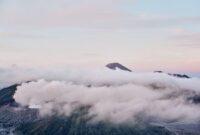 Pemandangan kabut tipis yang menyelimuti lembah hijau pegunungan Indonesia saat terbit fajar, menyajikan suasana tenang bagi para pelancong pencari ketenangan jiwa.
