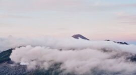 Pemandangan kabut tipis yang menyelimuti lembah hijau pegunungan Indonesia saat terbit fajar, menyajikan suasana tenang bagi para pelancong pencari ketenangan jiwa.