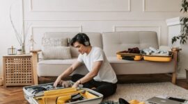 Seorang pelancong sedang menyusun pakaian dan perlengkapan secara rapi ke dalam koper ransel dengan konsep efisien sebelum memulai perjalanan liburan yang menyenangkan.