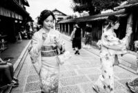 Suasana tenang di salah satu lorong bersejarah di kawasan Gion, Kyoto, di mana para pejalan kaki dapat merasakan kehangatan arsitektur kayu tradisional di tengah rinai hujan tipis.