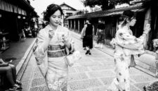 Suasana tenang di salah satu lorong bersejarah di kawasan Gion, Kyoto, di mana para pejalan kaki dapat merasakan kehangatan arsitektur kayu tradisional di tengah rinai hujan tipis.