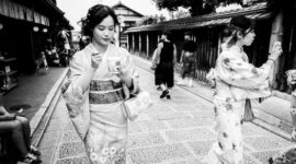 Suasana tenang di salah satu lorong bersejarah di kawasan Gion, Kyoto, di mana para pejalan kaki dapat merasakan kehangatan arsitektur kayu tradisional di tengah rinai hujan tipis.