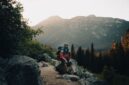 Seorang petualang berdiri menatap pemandangan pegunungan saat matahari terbit, menggambarkan keindahan alam liar yang menjadi tujuan utama para pejalan mandiri modern.