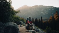 Seorang petualang berdiri menatap pemandangan pegunungan saat matahari terbit, menggambarkan keindahan alam liar yang menjadi tujuan utama para pejalan mandiri modern.