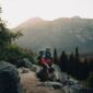 Seorang petualang berdiri menatap pemandangan pegunungan saat matahari terbit, menggambarkan keindahan alam liar yang menjadi tujuan utama para pejalan mandiri modern.