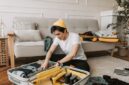 Seorang pelancong sedang menata pakaian secara rapi dengan teknik gulung ke dalam koper berukuran sedang untuk efisiensi ruang perjalanan.