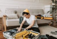 Seorang pelancong sedang menata pakaian secara rapi dengan teknik gulung ke dalam koper berukuran sedang untuk efisiensi ruang perjalanan.
