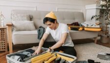 Seorang pelancong sedang menata pakaian secara rapi dengan teknik gulung ke dalam koper berukuran sedang untuk efisiensi ruang perjalanan.