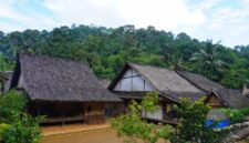 Seorang pelancong menikmati pemandangan perbukitan hijau Sumba sembari berinteraksi dengan warga lokal di sudut desa adat yang tenang.