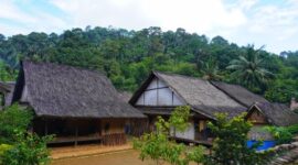 Seorang pelancong menikmati pemandangan perbukitan hijau Sumba sembari berinteraksi dengan warga lokal di sudut desa adat yang tenang.