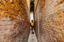 Seorang penjelajah mandiri melangkah menyusuri lorong berbatu di kawasan bersejarah kota tua Eropa sambil menikmati suasana sore yang tenang.