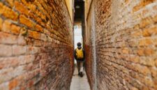 Seorang penjelajah mandiri melangkah menyusuri lorong berbatu di kawasan bersejarah kota tua Eropa sambil menikmati suasana sore yang tenang.