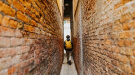 Seorang penjelajah mandiri melangkah menyusuri lorong berbatu di kawasan bersejarah kota tua Eropa sambil menikmati suasana sore yang tenang.