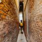 Seorang penjelajah mandiri melangkah menyusuri lorong berbatu di kawasan bersejarah kota tua Eropa sambil menikmati suasana sore yang tenang.