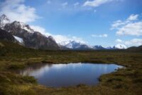 Seorang pendaki berjalan menyusuri jalur terjal dengan latar belakang puncak es dan danau alpine di kawasan Patagonia. Pemandangan lanskap murni ini menjadi salah satu daya tarik utama petualangan alam terbuka kelas dunia.