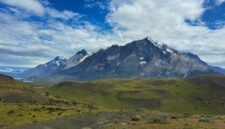 Seorang pendaki menikmati panorama keindahan puncak granit dan danau es di Taman Nasional Torres del Paine, Chili, yang menjadi salah satu destinasi petualangan terbaik dunia.