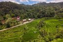 Pemandangan pedesaan tradisional di Sumba dengan latar belakang perbukitan hijau dan rumah adat beratap tinggi yang menawarkan suasana tenang bagi para pelancong.